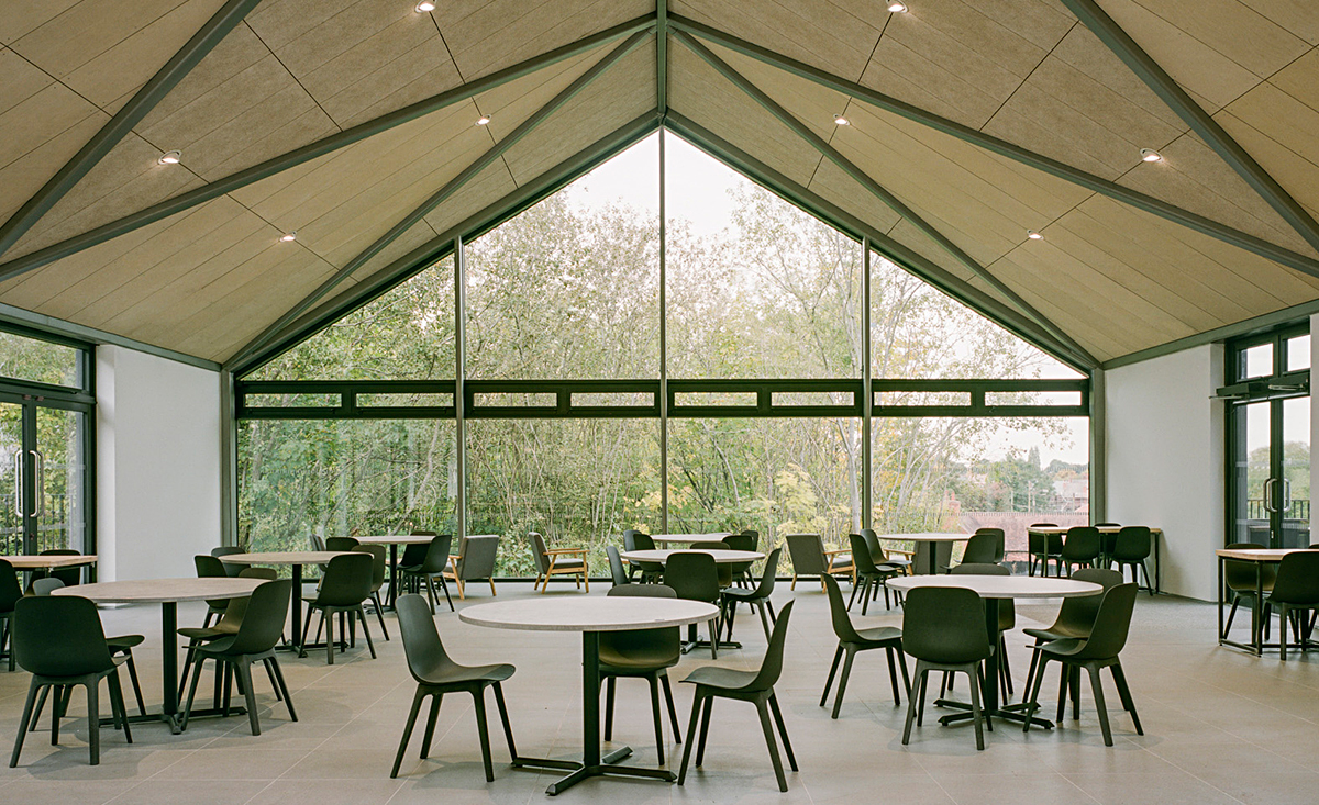 Café seating area in one of the vaulted ceiling volumes with a fully glazed view onto the wooded landscape.